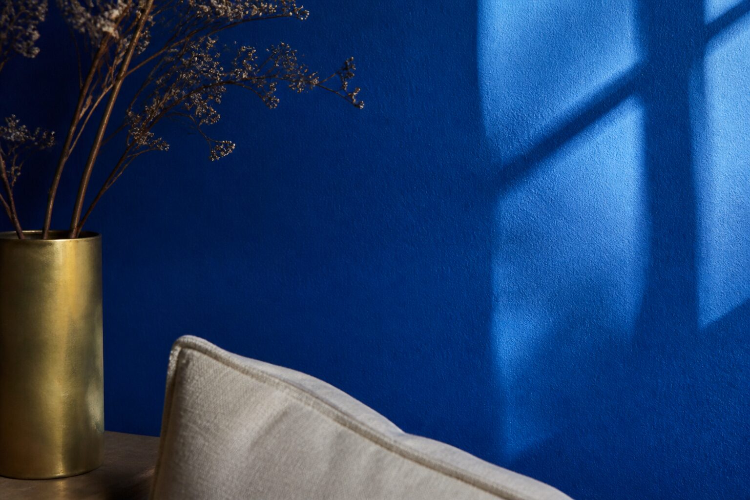 Gros plan sur un mur peint en bleu roi intense avec un reflet de lumière naturelle de fenêtre, texture mate légèrement granuleuse, palette bleu profond et lin